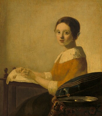 Painted almost entirely in tones of golden, mustard, and pale yellows, a young woman is shown from the lap up having turned to face us while making lace on a wooden frame in this vertical portrait painting. Her body faces our left almost in profile, but she turns her face to look at us with large, hazel-gray eyes. Her skin has a yellow cast but her smooth cheeks are lightly flushed, and her coral-red lips are parted. Her cinnamon-brown hair is parted down the middle and pulled back under a slate-blue ribbon, and she wears a teardrop-shaped earring in the ear we can see. Her burnt-orange shirt has pale yellow, wide cuffs at the elbow-length sleeves and a wide collar that rests across her chest and shoulders. The cuffs and collar are textured, suggesting fur. She rests her bare forearms against the wood frame in front of her, to our left, which is about the height of a table. A parchment-yellow cloth is draped over the frame, and she holds two short, cylindrical bobbins in her hands. Two more thread-wrapped bobbins hang to one side. The woman’s tea-brown skirt is partially hidden by a table situated closer to us, in the lower right corner of the painting. The table is covered with a patterned rug in maroon red, black, and gold. On the table are a low, wide pewter-gray bowl and a dark indigo-blue pillow with gold tassels and gold stripes near the seams. The wall behind the woman is honey yellow.