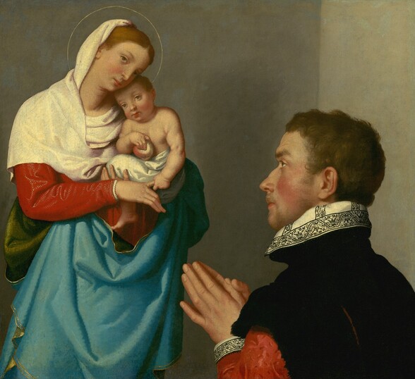 A man standing to our right with his hands together in prayer faces a woman holding a baby to our left in this vertical painting. All the people have pale skin. In the lower right quadrant of the painting, the man is shown from the chest up and is angled away from us so his profile faces our left. He has short, wavy brown hair, a bumped nose, flushed cheeks, and a faint goatee. He wears a black jacket with crimson-red sleeves. The high white collar and cuff of the hand we can see is decorated with a scrolling pattern in black. Slightly smaller in scale, the woman to our left is shown from the knees up. She wears a cherry-red dress under a cream-white mantle draped around her head and shoulders. A gold-edged, robin’s egg-blue drapery with a forest-green underside wraps around her middle and falls from the area of her waist. She stands with her body facing us and her head tilted to our right toward the baby in her arms. She looks up and to our left with brown eyes. She has brown hair, a straight nose, and her small pink lips are closed. Her head is encircled with a gold line indicating a halo. The baby she holds leans his head against her shoulder and looks off to our left, also with brown eyes. He has rounded cheeks and a chubby chest and arms. His midsection is wrapped with a white cloth, and he holds a yellow and red apple with his right hand, on our left. With his other hand, he holds the woman’s pointer finger. The scene takes place near the corner of a room with parchment-white walls.