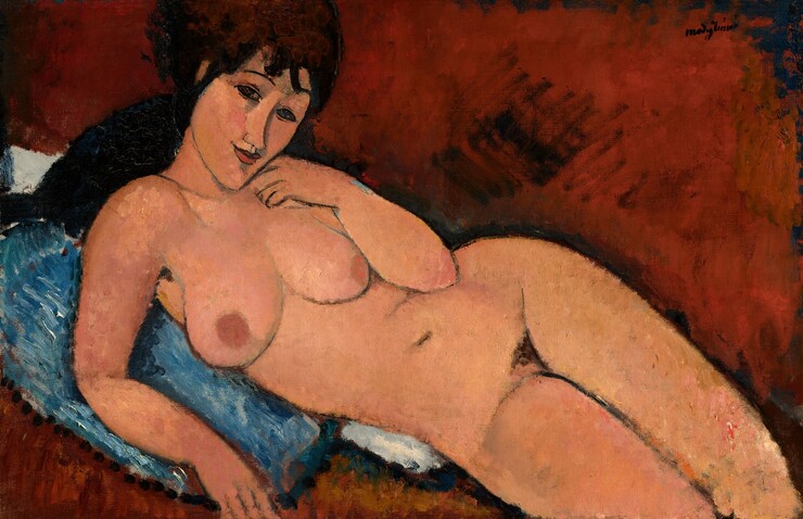 A nude woman with long, dark brown hair and peach-colored skin reclines against a denim-blue cushion in this stylized, horizontal painting. The painting is done mostly with areas of mottled color outlined in delicate black lines. Shown from the knees up, the woman lies with her legs to our right, and her hips tipped forward so her body faces us. She looks at us with dark, almond-shaped eyes under thin, arched brows. Bangs gather across her forehead, and her dark hair seems to be pulled back. Her head is tipped to our right, and she has an upturned nose, smooth cheeks, a pointed chin, and her smiling coral-red lips are closed. She holds the back of her left hand to her cheek and props herself up on her other elbow. Her rounded breasts have rust orange-colored nipples, and the contours of her body are smooth. There is a patch of dark hair at her groin, and her legs are pressed together. The blue pillow she rests on overlaps a white cloth or second pillow. The rest of the background is painted a terracotta brown with loose brushstrokes, so the setting is undefined. The artist signed the painting in dark letters in the upper right corner: “modigliani.”