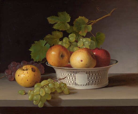 A speckled yellow apple and bunches of purple and green grapes are arranged next to an intricately pierced white bowl piled with more apples and grapes in this almost square still life painting. The objects sit on a sand-colored stone ledge, and the fruit gleams in bright light coming from the upper left. Sitting to the left of the basket, the yellow apple has brown spots and a worm hole near the top. In front of it, the green grapes partially cascade over the front edge of the ledge. The purple grapes lie in the shadow behind the apple. The white bowl has a wide, flaring mouth rimmed with dark blue, and sits to our right of center. It is pierced with four rows of narrowly spaced, undulating waves that spread out from a central eight-sided medallion. One red and two more yellow apples, one of which also has a small wormhole, sit along the lip of the bowl. They are topped by a cluster of green grapes framed by green leaves and a stem that angles into the upper right corner of the painting. The background is silvery gray to our right, where the light falls, and is in black shadow in the upper left.