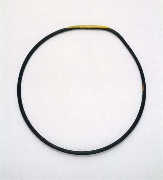 A dark-colored hoop, perhaps black, is shown against a white background. A sliver of lemon yellow is painted across the top edge of the hoop. The nearly perfect symmetry of the circle is broken only by a slight bend on the upper right.