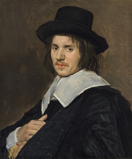 Shown from the chest up, a pale-skinned man holds one hand to his chest as he looks at us in this vertical portrait painting. His body is angled to our left almost in profile, and he turns his head to gaze out from the corners of his dark brown eyes. He has thick, dark brows, fleshy cheeks, and his pink lips are parted. He has a moustache and small patch of hair on under his lower lip. He has chin-length, straight brown hair and wears a high-crowned, brimmed black hat pushed slightly back on his forehead. A flat white collar lies across his shoulders over a voluminous black coat. His right palm, farther from us, rests against his chest, and the other hand is tucked below, mostly hidden by the coat. The wrist we see has a wide white cuff. The portrait is loosely painted, especially in the black-on-black pattern of the man’s clothing and the earth-brown background. The artist signed the painting with his initials in a conjoined monogram near the man’s far elbow, along the left edge of the canvas: “FH.”