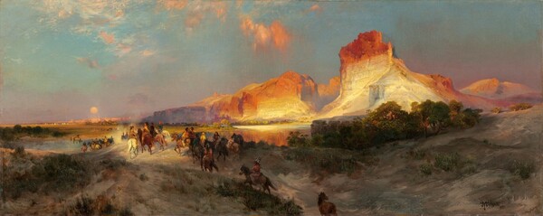 Sheer, vertical, cliffs, brightly lit in cream white and rust orange by the low sun, tower over a band of people riding horses into the distance in this long, horizontal landscape painting. The glowing cliffs dominate the upper right quadrant of the painting. They lighten from burnt orange along the jagged tops to flame orange down the steep sides, and are and warm, parchment white near the earth. One tall, narrow promontory to our right looms over a range of lower, rounded cliffs. As the cliffs move into the distance, they are shrouded with a lavender-purple haze. The land closest to us dips into a shallow valley at the bottom center of the composition, leading away from us. The dirt-packed earth is dotted with pine-green, scrubby bushes and vegetation and a grove of low, gnarled trees a short distance to our right. One chestnut-brown horse walks along the path at the bottom center of the composition, lagging behind a cluster of at least two dozen horses and riders winding into the distance. The horses range from ivory white to tawny brown and charcoal gray. The riders are loosely painted so some details are indistinct, but they all seem to have brown skin and dark hair. They wear feathered headdresses and garments in teal blue, fawn brown, or golden yellow. They ride over a low hill toward a crystal-blue river, and then back along a flat expanse toward a row of miniscule, triangular tepees lining the horizon in the deep distance. The horizon comes halfway up the composition, and the tepees are backed by a row of rose-pink, flat-topped cliffs. A pale yellow disk hangs low in the sky, over the distant cliffs. The sky above deepens from soft, lilac purple along the horizon to ice and sapphire blue along the top. A few wispy clouds are burnished orange in the sunlight. The artist signed and dated the painting in the lower right corner, “TYMoran 1881,” with the T, Y, and M overlapping to make a monogram.