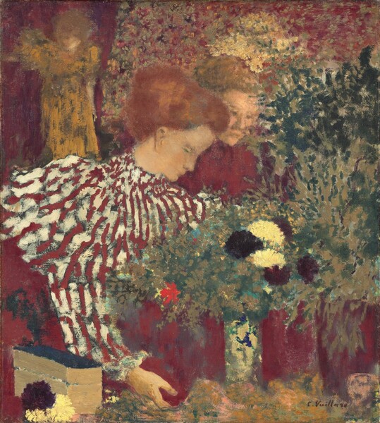 Two pale-skinned women are shown from the waist up behind a counter in an interior space in this nearly square painting. Loosely painted patterns on their clothing, bunches of flowers to our right, and the background to our left create a patchwork of claret red, ivory white, forest green, deep burgundy, and golden yellow. The woman standing closer to us takes up the left half of the composition. She faces our right in profile. Her features are painted with blended strokes so are indistinct. Her auburn hair is pulled up, and her high-collared, garnet-red and white striped shirt has long sleeves with puffy shoulders. She looks down at a red vase of flowers she holds at its base with the hand we see. The second woman stands at the first woman’s far shoulder. She turns her face slightly toward us, and also gazes down at the flowers on the counter. Her high-necked shirt is ruby red. Four wine-red vases in front of the women are filled with dark maroon-red or cream-white flowers, perhaps chrysanthemums, forest-green and tan greenery, and one vivid, tomato-red blossom. A gap between two vases could be another vase either patterned with white and celestial blue or reflecting those colors. A dark red and two white blossoms are in the lower left corner of the composition, next to a long, lidded box with light brown sides and a navy-blue top. A loosely painted form in the upper left corner, over the first woman’s shoulder, could be a figurine or another person. Though the details are vague, there is a suggestion of a face turned leftward. She has blond hair and wears a long, loose marigold-yellow garment. The right arm, to our left, could be raised to shoulder height, and she stands before a crimson background, maybe a curtain. The rest of the background is painted with dots and touches of apple red, maroon, orange, sage green, dark brown, and butter yellow. The artist signed the canvas near the lower right corner, “E. Vuillard.”