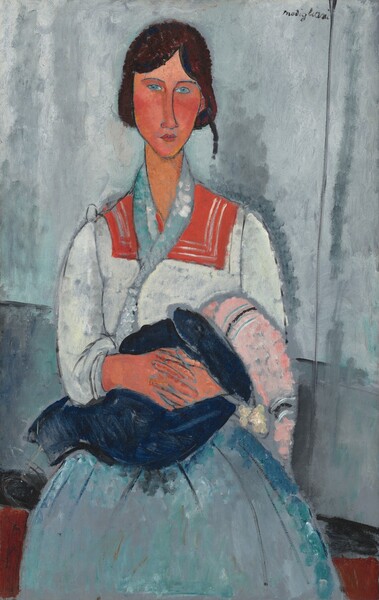 Shown from the knees up, a woman with peach-colored skin and dark hair sits facing us and holding a baby in this stylized, vertical portrait painting. The woman’s features are elongated and simplified, and the nearly geometric forms are outlined with gray. Loose brushstrokes are visible throughout, creating a textured, mottled effect. The woman’s long, thin face comes to a point at her chin, and her brown hair is pulled back on either side of her forehead. She has pale blue eyes, an exaggeratedly long nose, noticeably flushed cheeks, and her coral-pink, bow lips are closed. Her white blouse has a wide, tomato-red, squared collar that lies over her shoulders, and a thin, light blue scarf drapes around her neck and down her chest. Her long, full skirt is blended shades of violet purple and sky blue. The woman’s hands are clasped around a baby wrapped in a navy-blue blanket. The baby’s head is covered with a long pink cap with black and white bands at each end. The woman casts a narrow shadow against the gray wall behind her. Bands of elephant gray, black, and brown behind her across the bottom of the composition suggest an abstracted bench or seat she sits on. The artist signed the work in dark letters near the upper left corner: “Modigliani.”