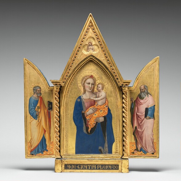 Two panels on a gilded, carved, wooden frame are swung open like shutters to show a bearded, gray-haired man wearing robes standing in each wing, on either side of panel with a pointed, arched top showing a woman holding a baby. In a three-lobed shape in the apex above the woman and child, a nude man crosses his arms over his chest. All the people have pale, ivory-colored skin. Gold halos encircle each person’s head and the background of all three panels is bright gold. The woman in the center panel is shown from the hips up with her body facing us. The deep blue mantle that drapes over her shoulders and her dusty rose-pink dress beneath are trimmed in gold. A sheer veil covers her wavy blond hair and a red, triangular form sits above her forehead like a diadem. She looks to our right with dark, almond-shaped eyes. She has a straight nose, her coral-pink lips are closed, and her smooth cheeks are lightly flushed with pale pink. She holds the child in the crook of her left arm, on our right, and rests her other hand in the baby’s lap. He has short, curly blond hair and looks directly at the woman. He reaches his right arm, farther from us, around his mother’s neck and hooks his other hand in the neckline of her dress. He wears a sheer shirt edged in gold, and the fabric draped around his hips is patterned with tangerine-orange and gold, with lapis-blue clover designs. He has rounded cheeks and a pudgy tummy, but his facial features and arms are scaled more like an adult. Twisted columns separate this central panel from the shutter-like panels to each side. A single person stands in each wing, filling most of the space, and both are angled and look towards the central panel. Both men have darker, olive-toned complexions, wear long robes trimmed in gold, and stand on floors patterned with orange, gold, and sparsely spaced royal blue diamond-shapes. The man to our left has short, steel-gray hair and a trimmed beard. Wrinkles line his forehead, and his brow is furrowed. He wears a topaz-blue, long sleeved garment under a honey-orange robe, the underside of which is ruby-red where it turns back over his wrists and shoulder. He holds a book with a dark cover up in his left hand, farther from us, and a large skeleton key in his other hand. In the right panel, a balding man has a fringe of long, gray hair and a flowing, full beard. His forehead is also creased with wrinkles and his brow is furrowed. The dark, olive-green lining of his rose-pink robe shows where it folds back at his neck, over his wrists, and down the front. His robe covers a topaz-blue garment as well. He holds a book, also with a dark cover, by his side with his left hand, closer to us, and holds up a feather quill with his opposite hand. The inner edges of each of the central panel and both wings are incised with bands of decorative floral and geometric designs punched into the gold backgrounds. In the pointed peak above the central panel, the nude man is shown from the waist up in a three-lobed, clover shape that would be visible even if the wings were closed. The man’s body faces us but his haloed head tips to his right, our left. He has a beard and long brown hair, and a hole dripping blood pierces the back of his left hand, visible on our right. The base of the tryptic is inscribed with gold letters in a dark field: “AVE GRATIA PLENA DO.”