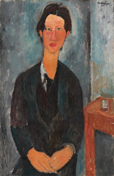 Shown from the lap up, a cleanshaven man with black hair and dark clothes faces us as he sits with his hands resting together in his lap in this stylized, vertical portrait painting. The man's features, clothing, and the room are painted with areas of mottled color with visible brushstrokes, so many details are indistinct. The man has peach-colored skin, and his facial features are outlined. He has dark eyes that look at us or slightly up, under thin, arched brows. One eye is a little higher than the other, and the two halves of his long face do not quite match. He has a wide nose, and his full, dark rose-pink lips are closed. His hair is parted down the middle and is brushed down to meet his ears. He has an elongated neck, and his narrow shoulders slope down. He wears black pants and a black coat over a dark teal-green vest. A white shirt is visible along his neckline, and an area of black could be the knot of a tie. He holds the fingers of one hand in his other, both hands resting in his lap. A loosely painted, brown table sits next to the man to our right, and an area of slate blue and white could be a glass on the table. A vertical line in the background behind the man, to our right, probably indicates the corner of the room. The walls are painted with strokes of smoke gray, ocean blue, and some parchment white. The artist signed the work in dark letters in the upper right corner, “modigliani.”