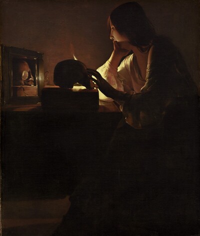 A young woman with pale skin sits at a table in a darkened room in this vertical painting. Long chestnut-brown hair drapes over her shoulder and her deep, cream-colored, long-sleeved garment is open at her neck. She rests her chin in her right hand, farther from us, as her left reaches for a skull placed on a thick book on the table in front of her. The scene is lit by a single candle mostly out of sight behind the skull. Shown in profile, she looks into a small mirror next to the skull, which reflects that object and the book.