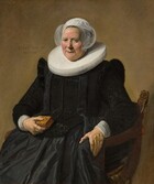 This vertical portrait shows an older woman wearing a full, long-sleeved, rich black dress with a wide white ruff at her neck and white lace cuffs at her wrists. She sits in a curving, low-backed wood chair against a pale brown background. Her body and the chair are angled slightly to our left and she looks directly at us. Her skin is fair, and she has small eyes, pink, rounded cheeks, and a wide chin. Her lips are parted in a slight smile and her hair is covered by a starched, sheer white cap that flares at the sides. The ruff around her neck is gathered in accordion-like, narrow figure-eight folds, and it extends flat and stiff, nearly to her shoulders. Close inspection reveals that the dress is woven with a black-on-black brocade pattern and has a line of small black buttons down the front. She holds a small brown leather book tooled with gold ornament in her right hand, on our left, and her opposite hand rests on the arm of the chair. She wears a gold ring on each hand. An inscription is painted to our left of her head: “AETAT SVAE 60 ANo 1633.” 