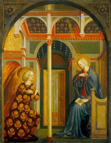 A winged angel with arms crossed kneels across from a young woman sitting and holding a book, both under an archway in a paneled room in this vertical painting. They both have pale, yellow-toned skin, blond hair, and flat, gold halos. They also have golden brown eyes, long, straight noses, smooth cheeks, and their pale, pink lips are closed. To our right, the woman sits in a throne-like chair with her body facing our left. Her head tilts down, and she looks toward the angel under lowered lids. Her hair is pulled back under the neck of the lapis-blue cloak she wears over a crimson-red dress. The dress and cloak are trimmed with gold, and a there is a gold starburst on the cloak over her left shoulder, closer to us. She holds her other hand up near that shoulder with her fingertips brushing her chest. With her other hand, she holds open the pages of a small book in her lap, so her fingers overlap some of the words. The entire inscription would read, “virgo concipiet et pariet filium et vocabitur nomen eius emmanuel butirum et mel come dit ut fiat reprobare.” A slender, bone-white column separates her from the angel opposite her, along the left edge of the painting. The angel has curly, shoulder-length hair and wears a robe with a gold, floral pattern against a burgundy-red background. Long, golden wings emerge from the shoulder blades and extend off the side of the composition. An open archway just beyond the angel is filled with streaks of flax yellow and burnt orange, possibly representing flames. Some of the walls in the room around the pair are pale olive green and other areas are darker spruce green. There are bands of coral-pink molding and inset panels of patterned mosaics. The flat ceiling of the space immediately over the pair is decorated with checkerboard panels in navy blue, hunter green, brown, and brick red. Gold lines create a ray coming from the ceiling toward the woman. At the back of the space, beyond the column separating the woman and angel, the room extends into an alcove with an arched hallway painted with gold stars against a midnight-blue background. Double doors open at the back of the alcove onto a room with a pale-yellow curtain with a mesh-like trim. We see the pair as if through a stone archway that lines the top and sides of the composition. The upper corners are filled with leafy decorations, as if carved into the stone.