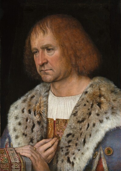 Shown from the chest up, a clean-shaven, pale-skinned man holds one hand to his chest and rests the other on a rug-covered ledge with the other in this vertical portrait painting. The man’s body is angled to our left, and he looks down in that direction with dark eyes under thick brows. Crow’s feet crinkle at the corners of his eyes, and there are dark hollows underneath. Soft jowls hang to create a slight double chin. His thin lips are set in a line over a wide, round chin, which is darkened with a five o’clock shadow. He has chin-length, reddish-blond hair, and straight, wispy bangs sweep loosely across his high forehead. He wears a white chemise under a gold, brocade garment, which is mostly hidden by a slate-blue cloak. The cloak is lined with spotted fur, which is turned over to create a wide collar across his shoulders. The sleeve on his left arm, to our right and closer to us, splits over a dusky-pink sleeve. Two gold buttons on the cloak there are decorated with thistle plants and blossoms. The fingers of his right hand, to our left, are gathered like a closed rose bud at his chest. He wears a gold ring on the index finger of the other hand, which rests on the end of the gray stone ledge so his fingertips brush the tapestry draped there. The man is lit from our left against a black background.