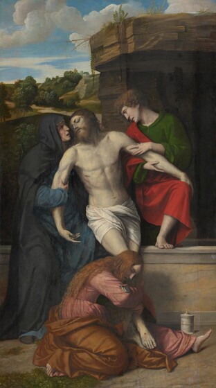 Two women and a man support the gray, lifeless body of a nearly nude man along a stone ledge in this vertical painting. The people have pale skin, except for the dead man at the center, Jesus, who has ash-white skin with dark shadows around his closed eyes. He has a long straight nose, and his lips are slightly parted. He has a brown beard, and his long, wavy hair falls away from his face. A white cloth wraps across his hips, and blood trickles from a gash over his right ribs and holes in his feet. A woman and man prop him up on either side, each holding Jesus by a limp arm, and each has a faint, gold halo encircling their heads. To our left, the woman holds her face close to his, her brows deeply furrowed and her mouth wide open, teeth showing. Her forehead, chin, and neck are covered by a white veil, worn under navy-blue cloak that covers her head and body. The cloak falls open over one arm and a bent knee to reveal her long-sleeved, lighter blue dress. On Jesus’s other side, a cleanshaven man with curly brown hair holds Jesus’s arm with both hands. The man’s eyes squint with tears as he tips his head toward Jesus. His pink lips are parted, and the corner of the mouth we can see is pulled down. He wears an emerald-green, long-sleeved tunic under a vivid red cloth that wraps around his right arm, waist, and left leg. The fourth and final person is a woman sitting on the ground, her arms wrapped tightly around Jesus’s crossed ankles. She sits with one foot tucked under her body and the other leg out straight. Waist-length, wavy, auburn-brown hair falls freely over her shoulders and across her face, but we can see her downturned, open mouth and nearly closed eyes. She wears a rose-pink dress, cinched at the waist. A brown cloth wraps around her waist and right leg. A cylindrical, lidded, white jar sits on the dirt ground nearby. The group is arranged in front a thigh-high stone ledge, except for the man in green and red, who steps into what is presumably the coffin. A rocky outcropping to our right has a cave-like opening with grasses and growth along the top. The landscape beyond has a dirt path winding between pine-green hills dotted with trees. Two slate-blue buildings perch atop one hill. White clouds float across the blue sky above.