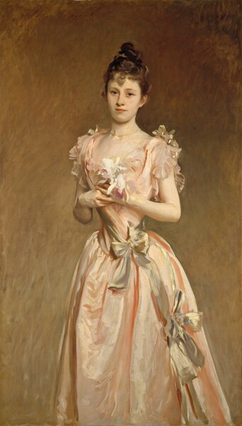 Shown from about the knees up, a young woman with pale skin, wearing a long, flowing, peachy-pink satin dress, looks at us in this vertical portrait painting. Her shoulders are slightly angled to our left, and she gazes out with dark gray eyes set in an oval face. She has a long, narrow nose, smooth skin, and her pink lips are closed. Her light brown hair is pulled up and twisted into a loose bun high on her head, and a curl hangs down the center of her forehead. A pearl necklace rests at the base of her neck. Her dress has a low, sweeping neckline and short, fluttering sleeves. The peach of the fabric almost blends in with the color of her skin in some areas. The dress has a tightly fitted bodice around a notably narrow waist, which is tied with a silvery gold sash. More golden bows are tied on her shoulders, and another farther down her skirt, near her left knee, to our right. The deep folds of her peach skirt are shaded with darker coral streaks. The two orchids she holds at her chest are mostly white but they have a couple of pale, lavender-purple petals, and each has a deep magenta-pink tongue. The background lightens from coppery brown along the top to a golden tan along the bottom. Some areas of the portrait are loosely painted, especially in the skirt and background. The artist signed the painting in the upper left corner, “John S. Sargent” and dated it in the upper right, “1890.”