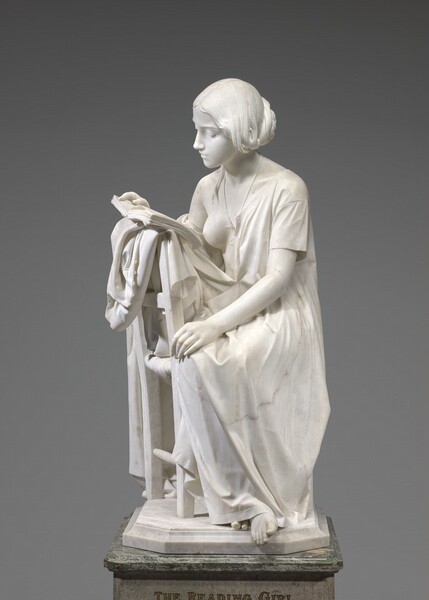 Carved from creamy white marble, a young girl sits turned to face the back of a wooden chair, where she props the open book she reads. In this photograph, her knees face us but her body and head are turned slightly to our left, towards the back of the chair, so we see her face almost in profile as she looks down at the book. Her long hair is loosely tied back at the nape of her neck. She has a straight nose and her lips are closed. A delicate tear falls from her left eye, closer to us. A short-sleeved garment like a nightgown falls open over her right shoulder so her breast is exposed. A medallion with a portrait of a man hangs from a long string around her neck. She holds the book open with her right hand, farther away from us, and her opposite hand rests in her lap. The book lies on more fabric bunching over the back of the straight wooden chair. Her bare feet, crossed at the ankle, peek out from under her long garment so that one foot extends beyond the marble base on which the chair rests.