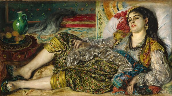 A woman wearing a sheer white blouse, short red and gold vest, and full-legged, patterned pants cinched below the knee lies back and looks at us with hooded eyes in this horizontal painting. Her shoulders lean back against an oversized white pillow, up along the right edge of the composition. Her body tips toward us, and her knees are bent so her feet are together in the lower left corner. Her right arm rests along the side of her body, and she props herself up with her other arm. That hand has a gold band on the ring finger. Her light skin is tinged with green on her face. Her head rolls slightly away from us so she looks down her cheeks at us with slitted, dark eyes through heavily lined lids. She has dark brows, and her rose-red lips are parted. The angle of her head creates a slight double chin. Gold hoops with dangling fringe or chains hang from her ears, and she wears three strands of dark beads around her neck. Her black hair is plaited in a thick braid that comes down over her left shoulder, closer to us. A cap made of gold-colored disks and red fringe sits on the far side of her head. The woman’s clothing is more loosely painted. We may see her breasts and pink nipples through her sheer, silver-gray tunic, which has long, voluminous sleeves. The short, bolero-style vest is strawberry red and gold, with narrow cap sleeves. A sea-blue sash around her waist is striped with overlapping burnt-orange and black lines. Her pants have flaring legs gathered with a button just below her knees. The pattern is of sage-green circles with swipes of rust-red in the center, suggesting flowers and vines against a black background. Her knees are spread open so her feet can barely be contained within the composition. Her teal-green slip-on shoes have the suggestion of flowers painted with dabs of yellow, black, and red, and a pompom atop each toe box. A red and gold cushion sits just beyond her feet. On it is a tray of oranges and an emerald-green jug. The pillow the woman leans on is propped against a short section of wall or piece of furniture painted with a border of roses. The room opens up beyond this, and has a turquoise and brown rug leading back to a cranberry-red sofa, on which a gray piece of fabric has been draped. The wall above is patterned with yellow and green diamonds and pink flowers against a laurel-green background. The artist signed the lower left, “A. Renoir. 70.”